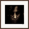A grainy, high-contrast portrait of a person with long, dark hair partially covering their face, looking directly at the camera. Framed with a dark border and signed in the corner, this piece brings mindful home decor to conscious interior design.