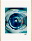 A close-up photo of the front door of an Electrolux washing machine features blue and green circular light reflections, making it perfect as inspirational wall art or mindful home decor. The artist’s signature appears in the lower right corner.