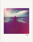 A silhouette of a person stands by the water under a cloudy sky. Soft, dreamy effects with purple and pink hues create inspirational wall art, perfect for mindful home decor. A signature appears in the bottom right corner.