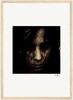 Sepia-toned close-up image of a person's face, partially obscured by shadows and dark hair, centered on a white mat with a light wood frame and a signature in the lower right corner. Perfect as inspirational wall art for conscious interior design.