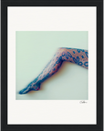 A person's leg extended horizontally in dark, floral-patterned lace tights against a light background, finished with a gallery-quality frame and a small signature in the lower right corner—perfect as inspirational wall art.