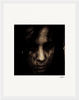 A dark, grainy close-up photo of a person's face with long hair partially covering it, set against a black background. The intense expression and signature on the white border make it a striking fine art print for conscious interior design.