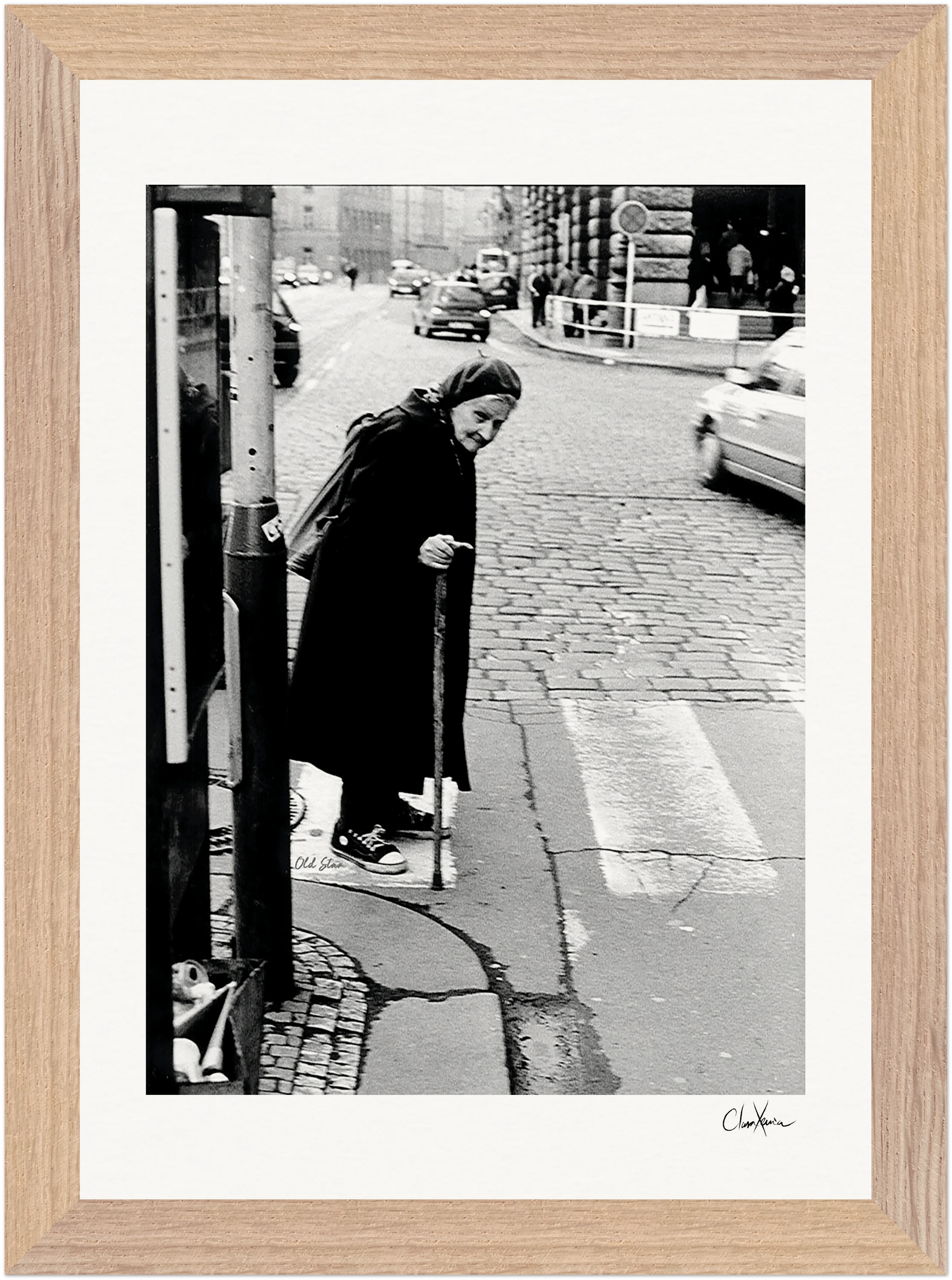 An elderly person wearing a headscarf and holding a cane stands at a street corner, gazing down at the cobblestone sidewalk. Cars and buildings line the background, creating an evocative scene perfect for inspirational wall art or fine art print.