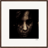 A close-up image of a person's face in dim lighting, partially obscured by shadows and strands of dark hair, photographed in a gritty, textured style. This framed wall art is centered on a white background with a dark frame.