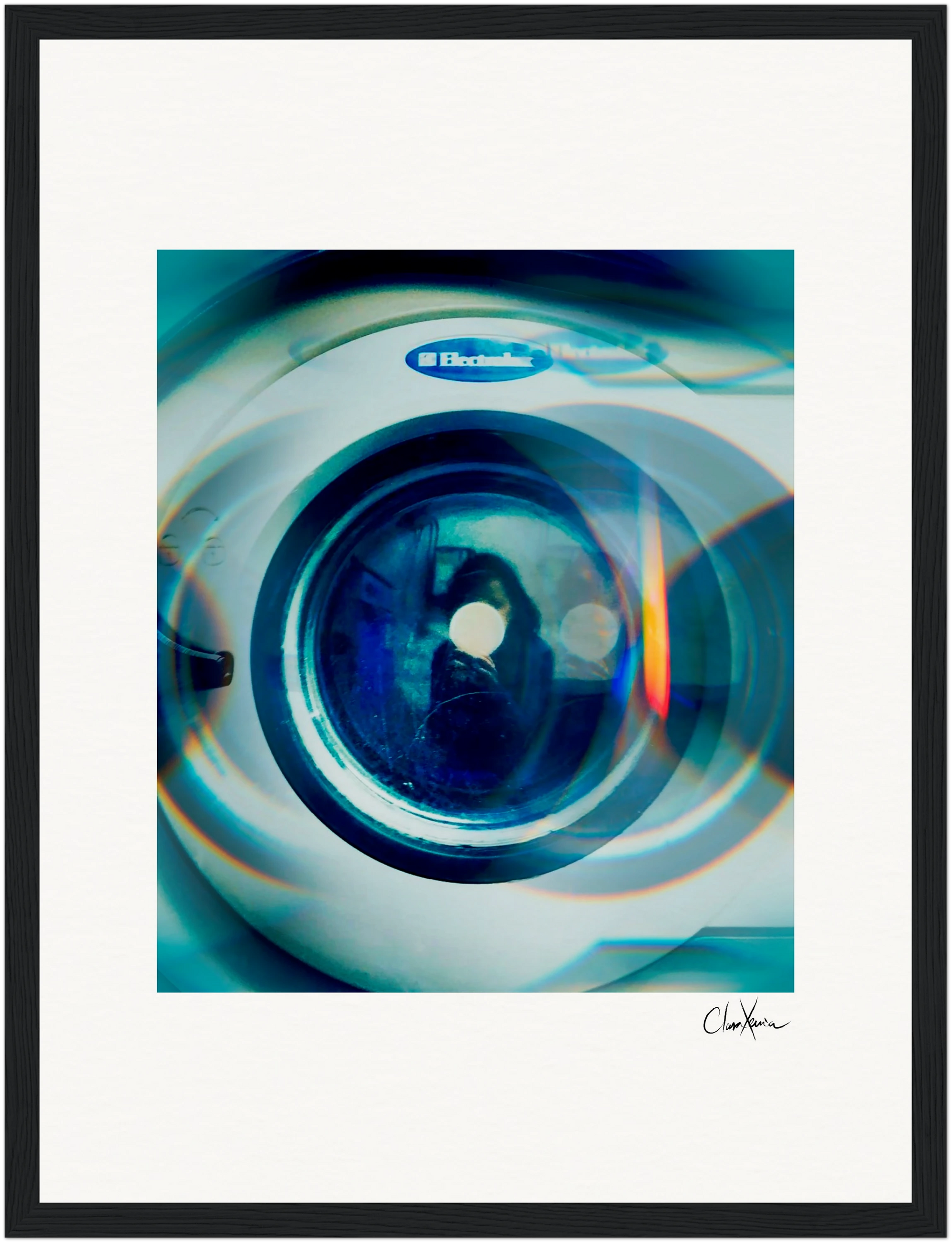 A framed fine art print of a washing machine door with light reflections and blue tones, featuring the Electrolux brand and an abstract reflection of a person. This inspirational wall art is signed in the bottom right corner.