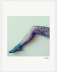 A single leg wearing floral-patterned lace tights is extended diagonally against a plain, light-colored background. This inspirational wall art features a white border and a small signature in the bottom right corner.