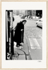 An elderly woman with a cane crosses a cobblestone street at a crosswalk, with cars and pedestrians in the background. This black and white scene makes for inspirational wall art that elevates mindful home decor.