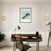 A modern home office featuring conscious interior design with a wooden desk, brown leather chair, black desk lamp, and mindful home decor. A fine art print of a patterned foot and ankle hangs above the desk, accented by wall sconces and a telescope.