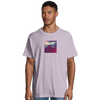 A man wears a light purple t-shirt featuring an art print of a colorful, abstract sunset on the chest, standing against a plain white background—perfect for those who value conscious fashion.