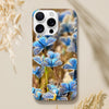 A smartphone with a case featuring an art print of blue butterflies on a natural background rests on a beige surface near dried grasses. The word “INTENTION” and a small symbol are printed at the bottom, adding artistic textures to the design.