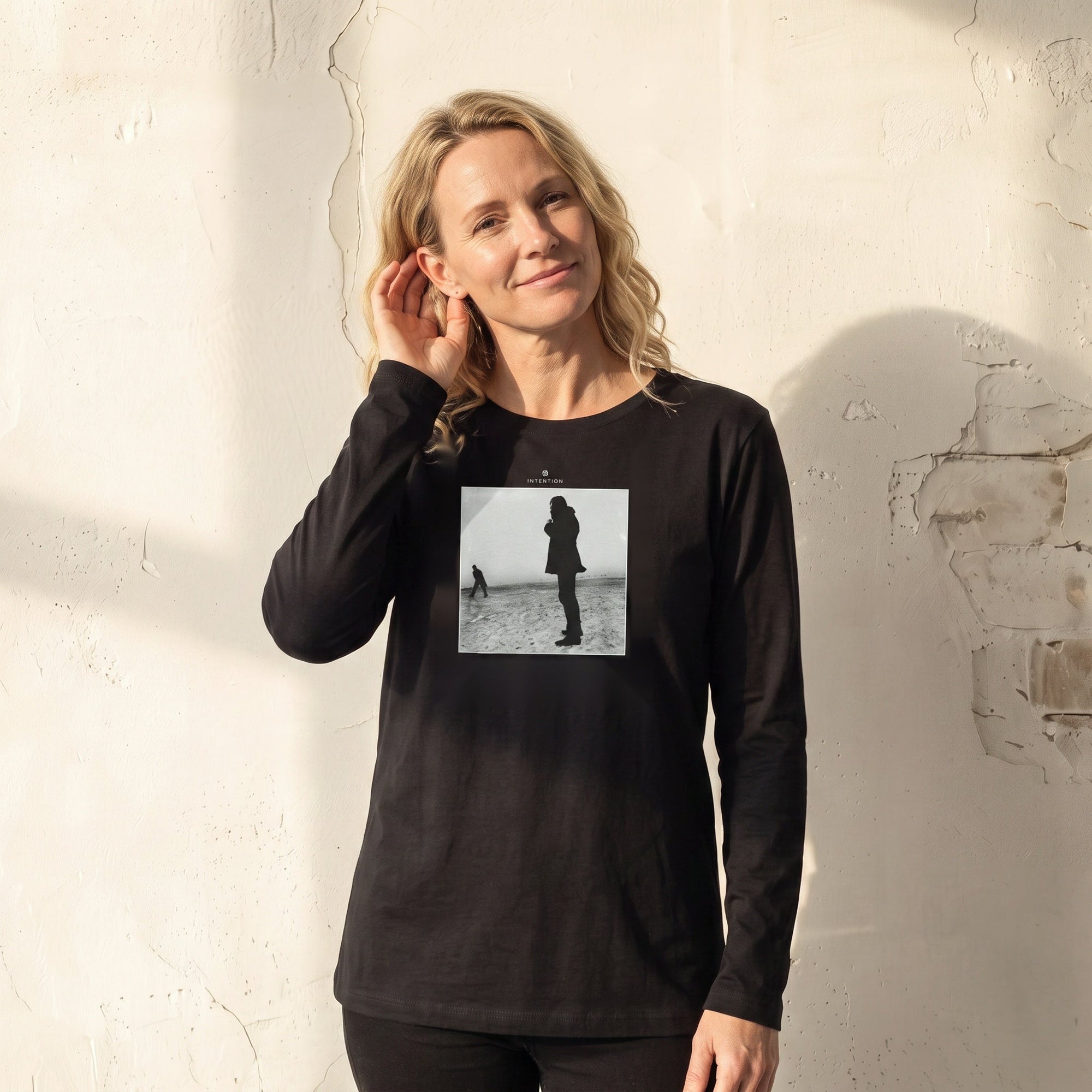Compassion - "The Space We Share" Deep Black Long Sleeve worn against a sunlit plaster wall