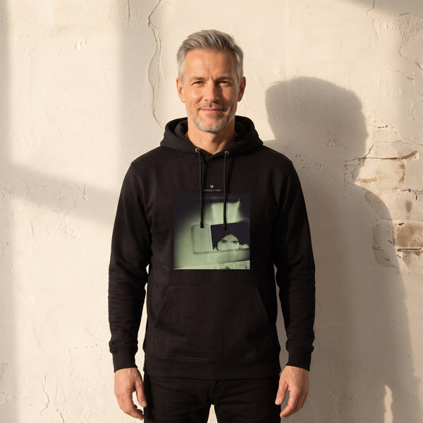 Curiosity - "On the Road" Black Hoodie worn against a sunlit plaster wall