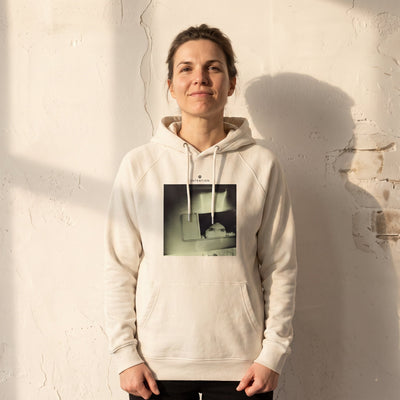 Curiosity - "On the Road" Off White Hoodie worn against a sunlit plaster wall