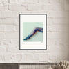 A framed photograph of a single outstretched leg in colorful, patterned tights is displayed as inspirational wall art on a white brick wall above a shelf with decorative dried flowers, perfect for mindful home decor.