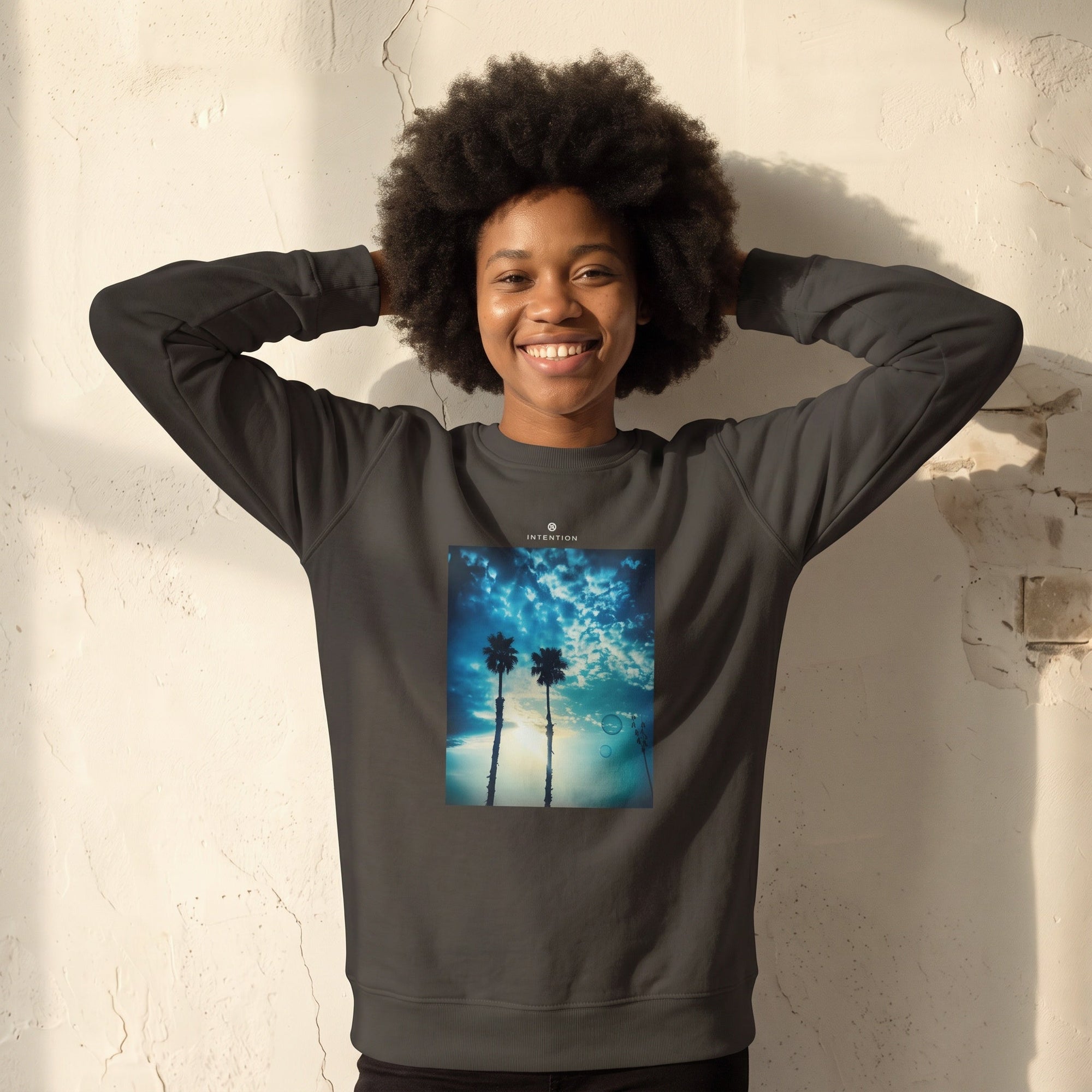 Gratitude - "Bubbles and Sky Sticks" deep charcoal grey Sweatshirt worn against a sunlit plaster wall