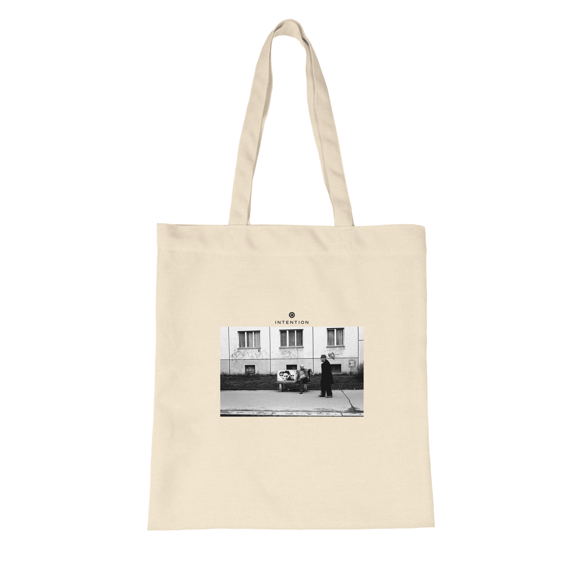 A natural tote bag made from organic material, featuring a black and white art print of a person walking past another sitting outside a building, with the word INTENTION printed above the image.