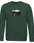 A bottle green crewneck sweatshirt features a centered black-and-white photo art print of a woman looking at the camera with text above, designed for conscious fashion enthusiasts.
