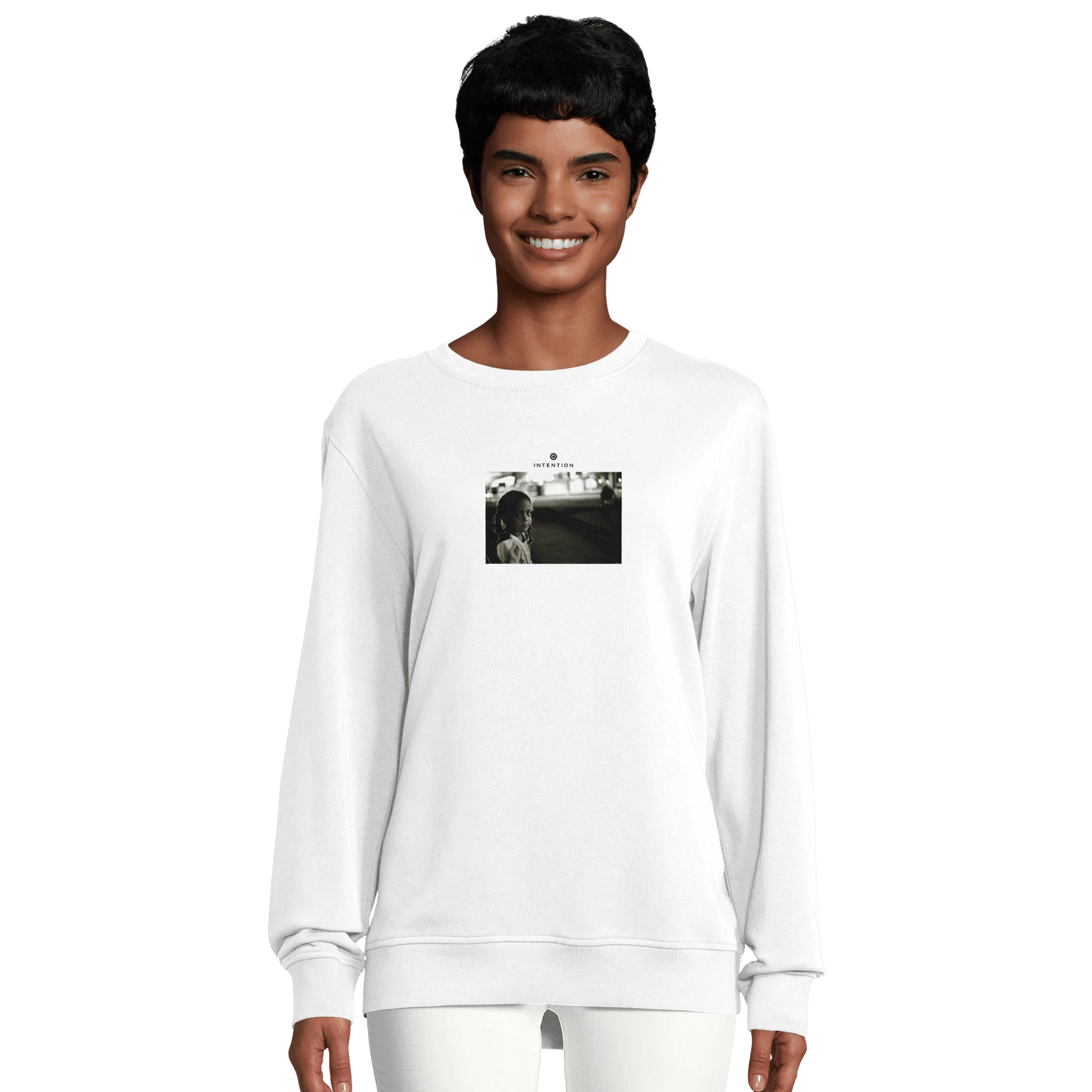 A person wearing a white sweatshirt featuring a small black and white art print on the chest. The photo shows people walking on a street, highlighting this piece of mindful apparel against a plain, light-colored background.