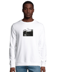 A man stands facing forward in a plain white sweatshirt featuring a small rectangular black and white photo on the chest. He pairs this mindful apparel with blue jeans, posed against a plain white background.