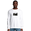A man stands facing forward in a plain white sweatshirt featuring a small rectangular black and white photo on the chest. He pairs this mindful apparel with blue jeans, posed against a plain white background.