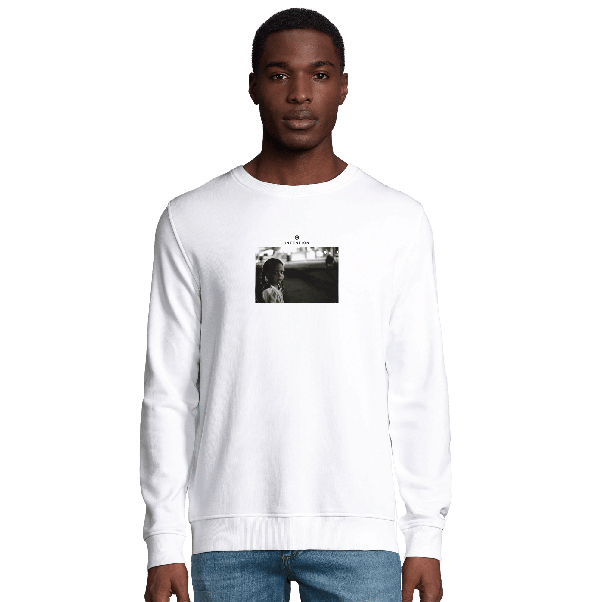A man stands facing forward in a plain white sweatshirt featuring a small rectangular black and white photo on the chest. He pairs this mindful apparel with blue jeans, posed against a plain white background.